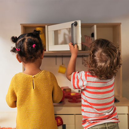 Two little kids playing in a miniature kitchen
